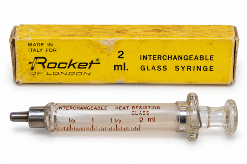 سرنگ شیشه‌ای قدیمی راکت لندن Rocket of London ساخت ایتالیا ظرفیت ۲ میلی‌لیتر با پیستون شیشه‌ای، اتصال فلزی و جعبه زرد اصلی